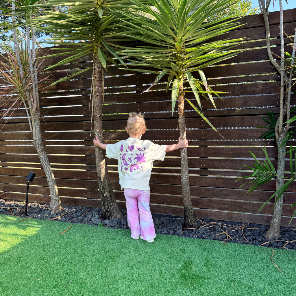 Toddler in the Cosmic Stardust Set with a Butter tee and pink tie-dye flares, showing the moon and star back print