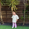 Smiling toddler tilting her head in the Butter Cosmic Tee and pink Stardust Flares