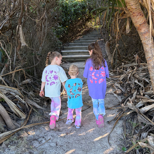Three kids walking a beach track in Cosmic Stardust Sets: Butter, Aqua and Grape Cosmic Tees with pink and blue tie-dye flares
