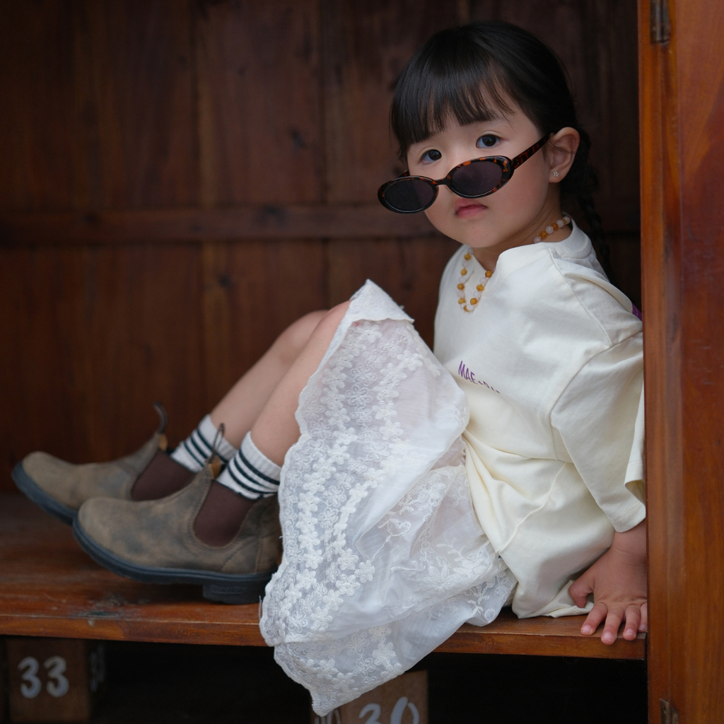 Girl in sunglasses wearing the Butter Cosmic Tee with a lace skirt, sitting in a wooden nook