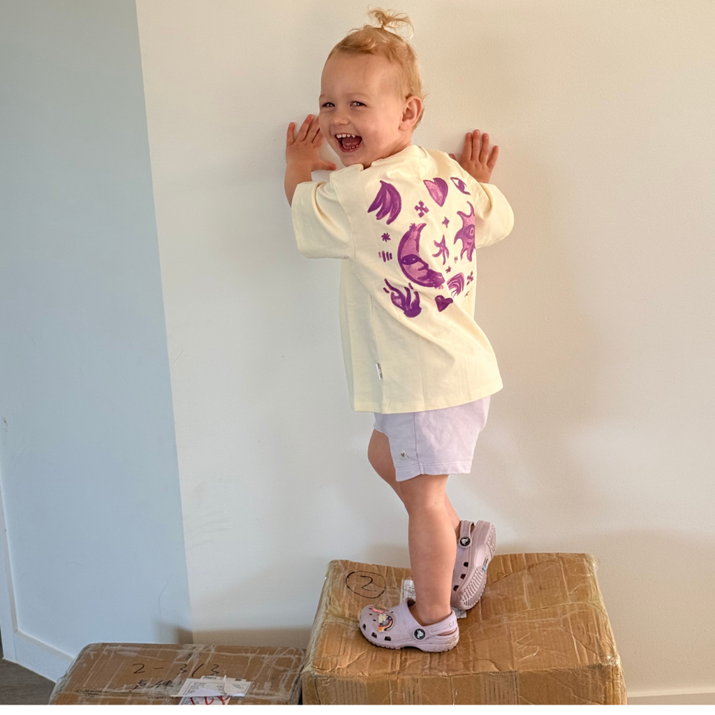 Laughing toddler wearing the Butter Cosmic Tee, showing the purple moon and star back print