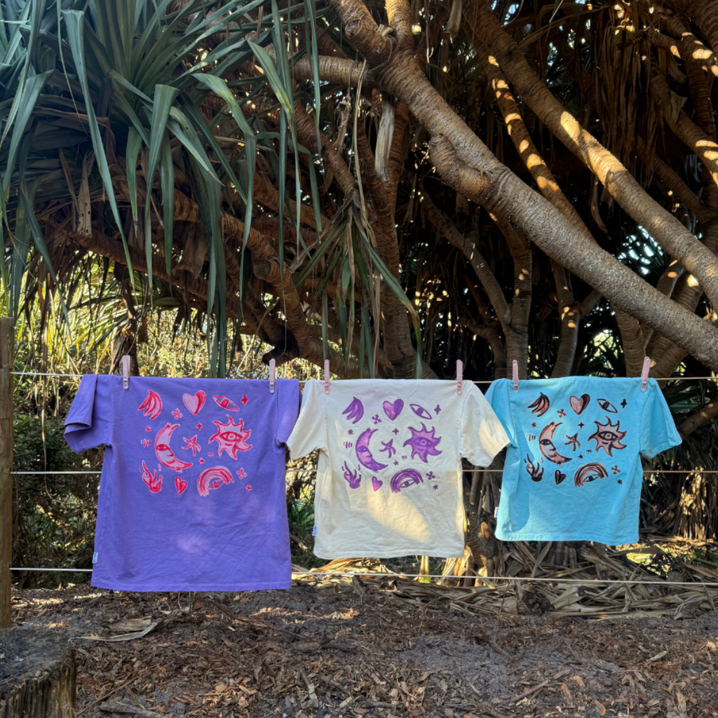 Cosmic Tees in Grape, Butter and Aqua hanging on a clothesline, showing the back prints