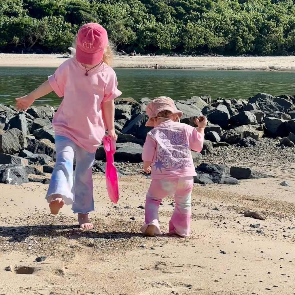 Two kids walking on the beach in Baby Pink Dreamers Tees, one in blue and one in pink Stardust Flares