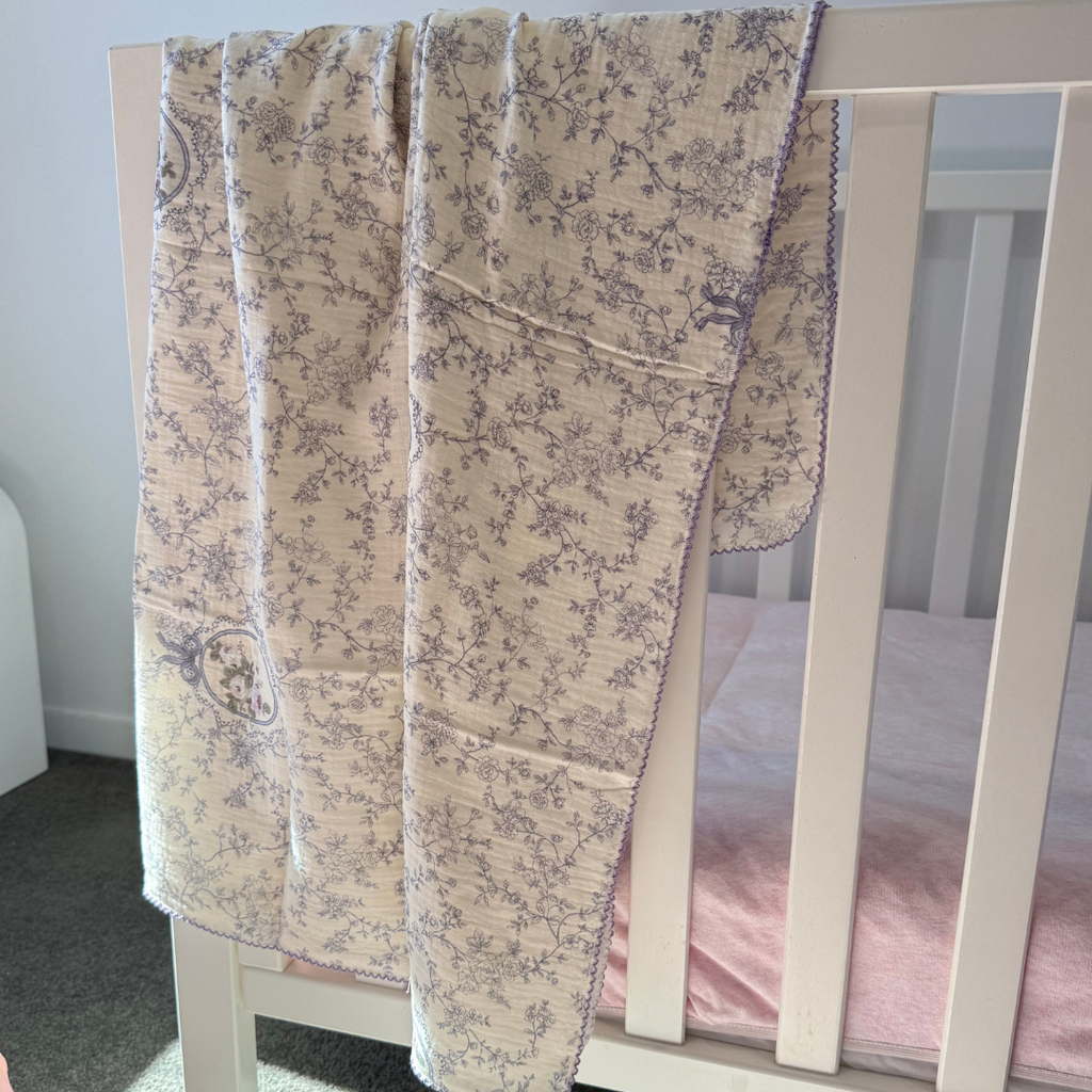 Lilac Vine crepe cotton swaddle with scalloped edge, draped over a white cot