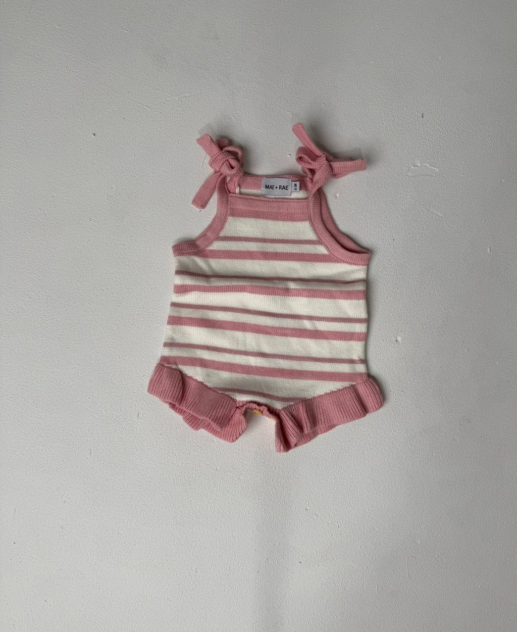 Lulu pink and white striped knit romper with tie straps and frill legs, laid flat