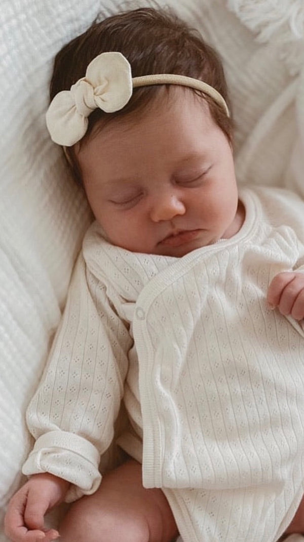 Newborn baby sleeping peacefully wearing a mae and rae pearl bow 